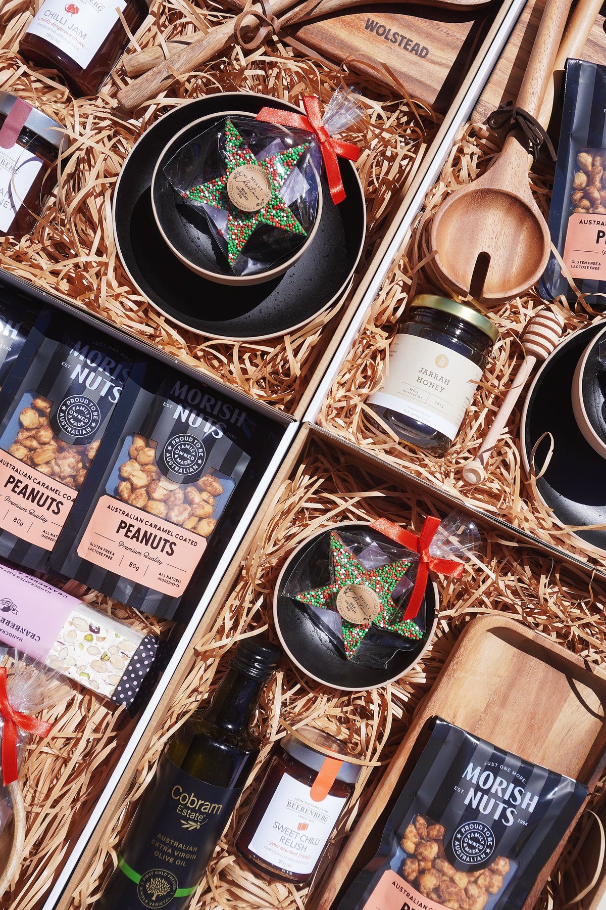 Overhead view of open corporate gift boxes filled with Morish caramel-coated peanuts, Jarrah honey, Cobram Estate olive oil and chilli relish on a wooden serving board, a Perth maker featured in No Matter What Gift Box corporate gift boxes